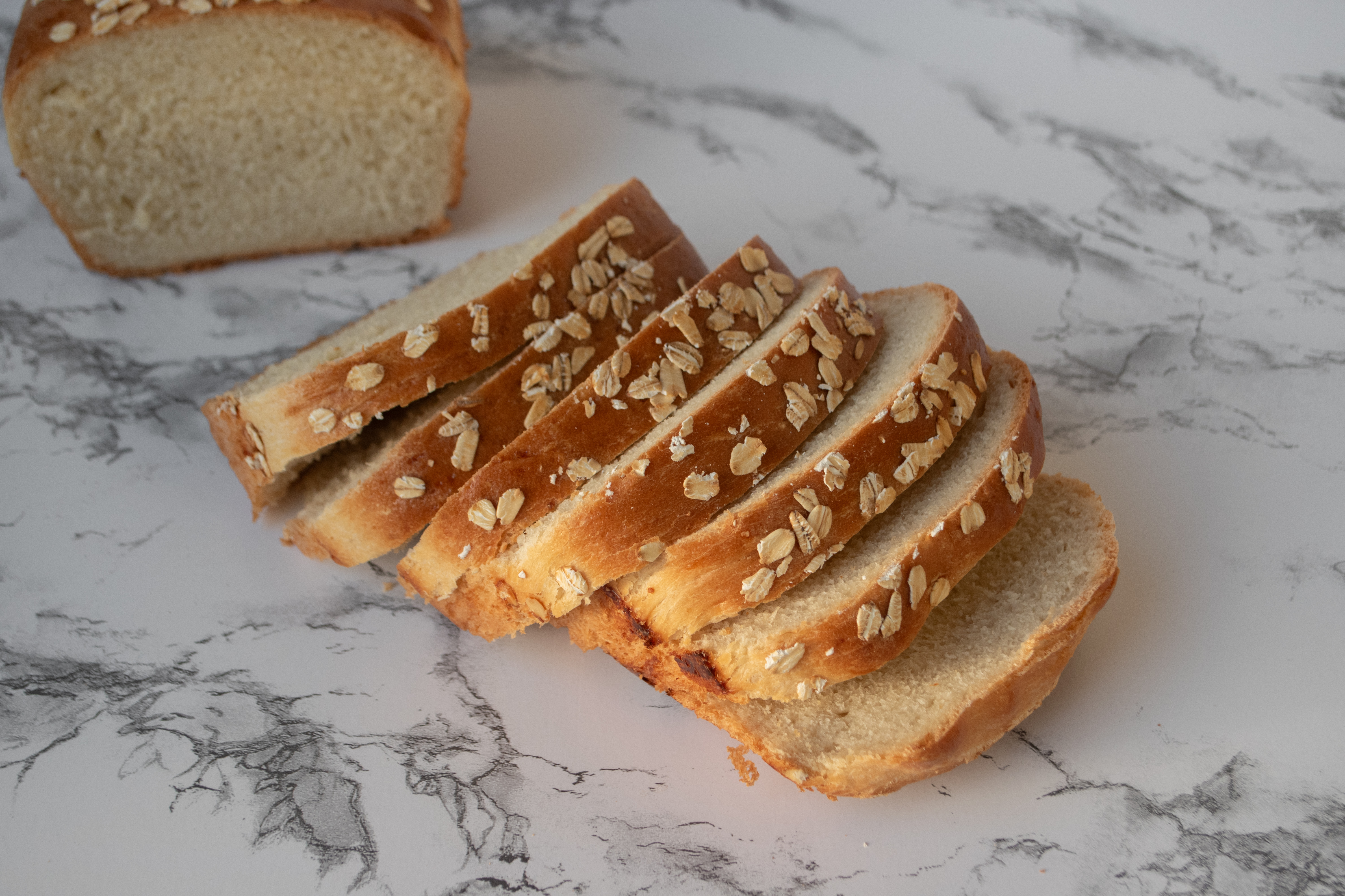 Slices of freshly baked bread topped with oats, placed on a marble surface.