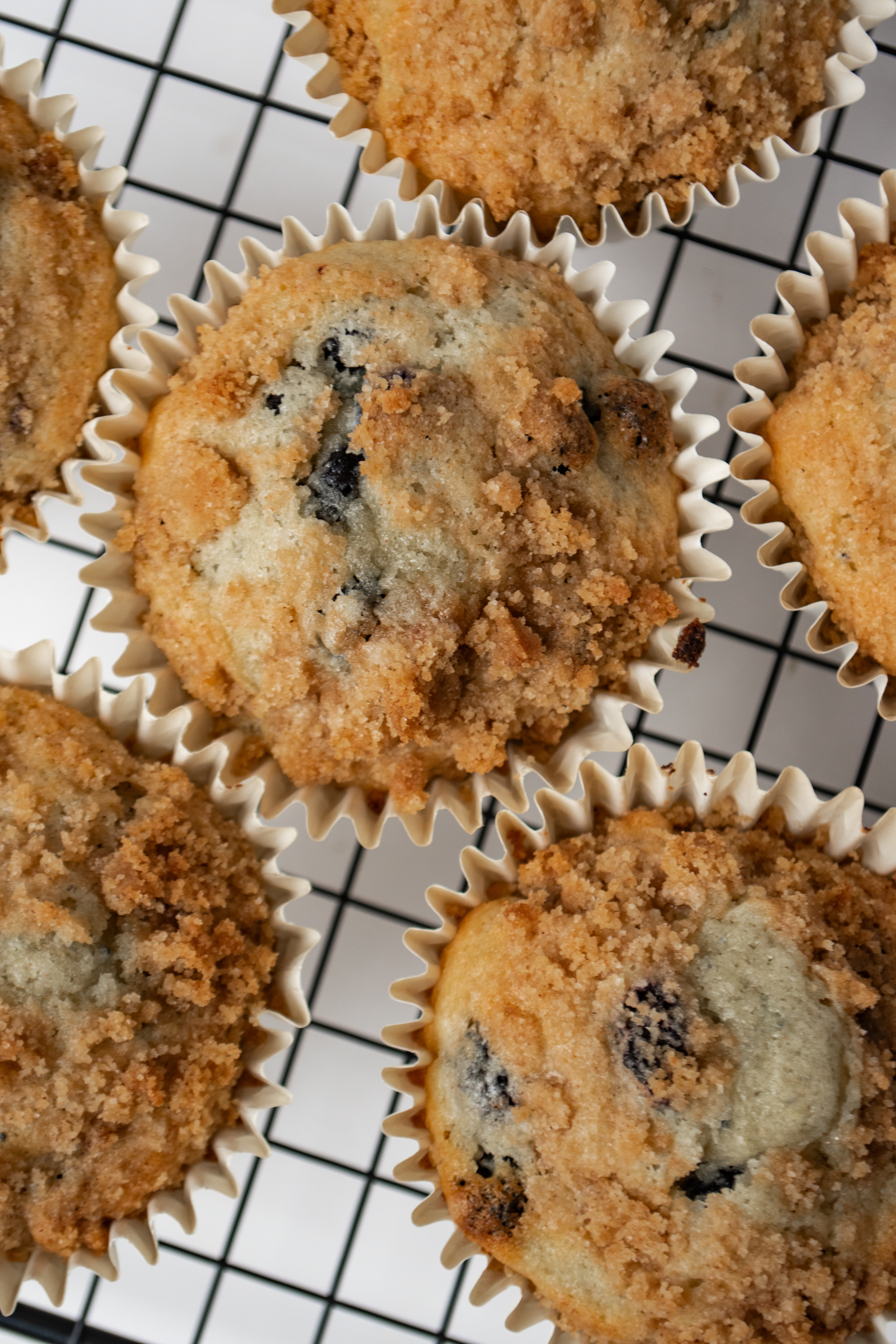 Freshly baked blueberry muffins with a crumbly topping, placed on a cooling rack.